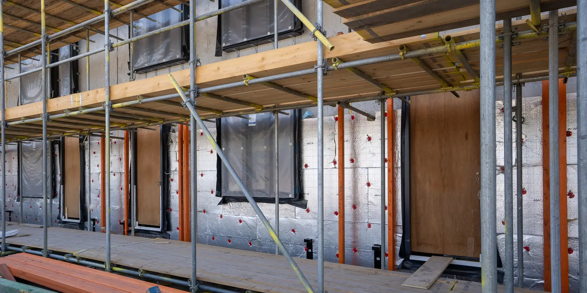 Insulation boards fixed across a house wall behind scaffolding