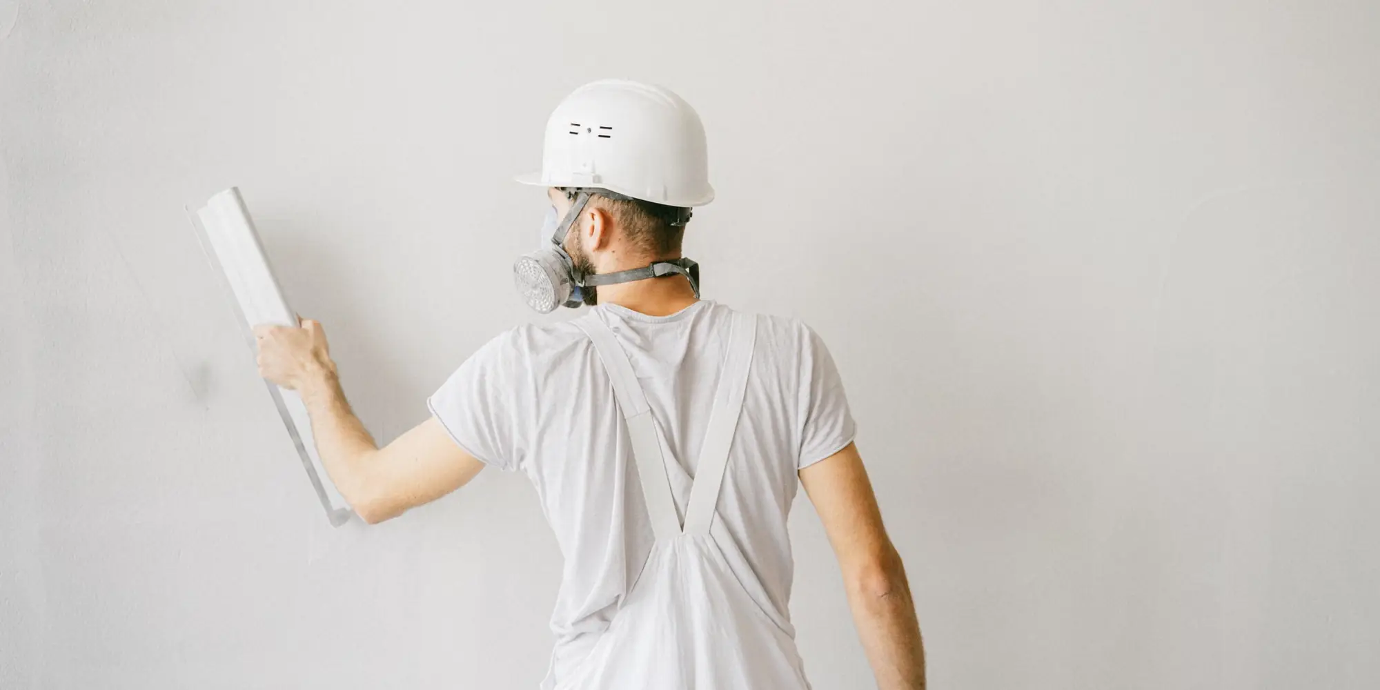 Plasterer in safety gear working a trowel across a white wall