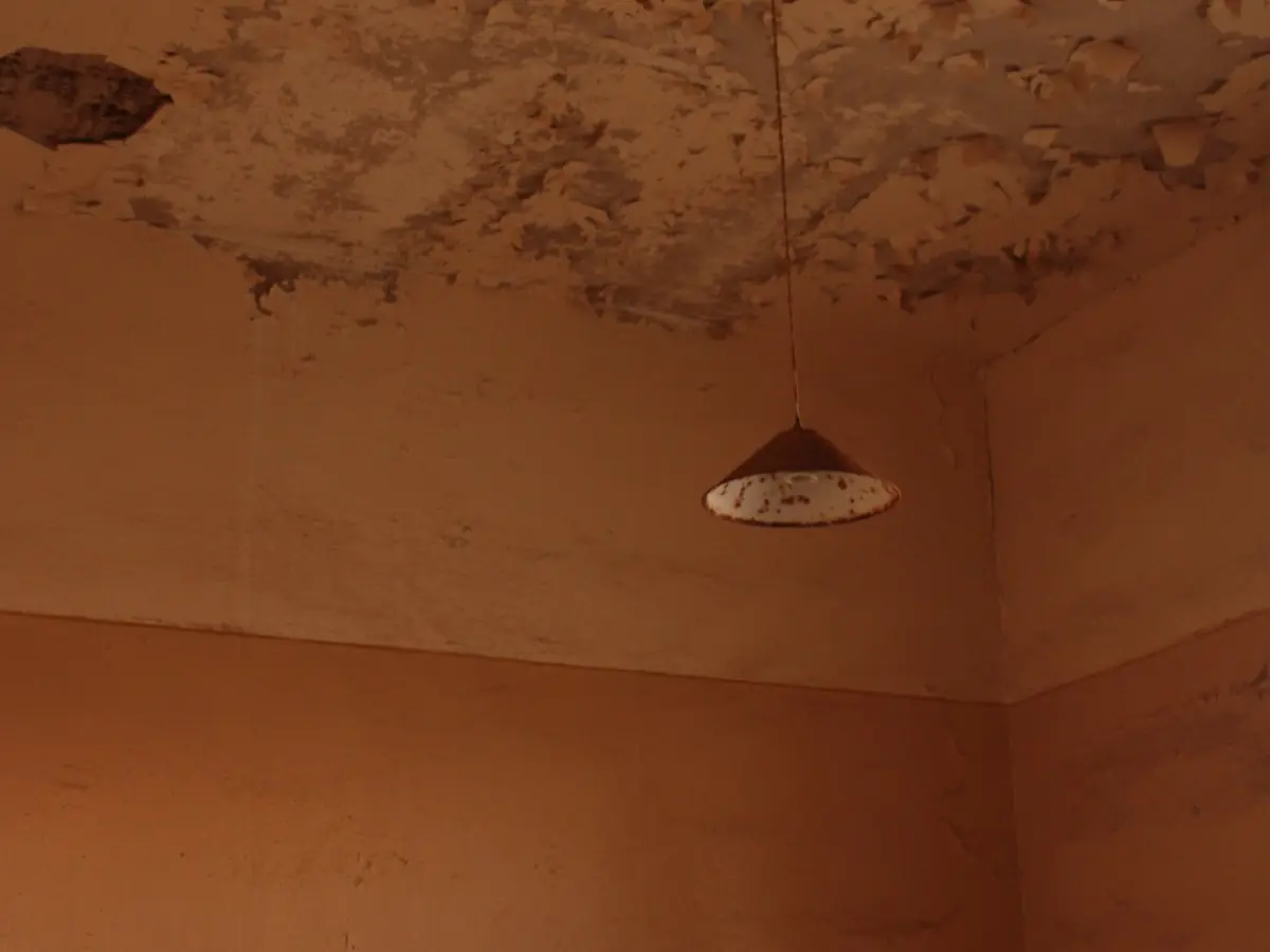 Worn ceiling with cracked plaster beside a hanging pendant light