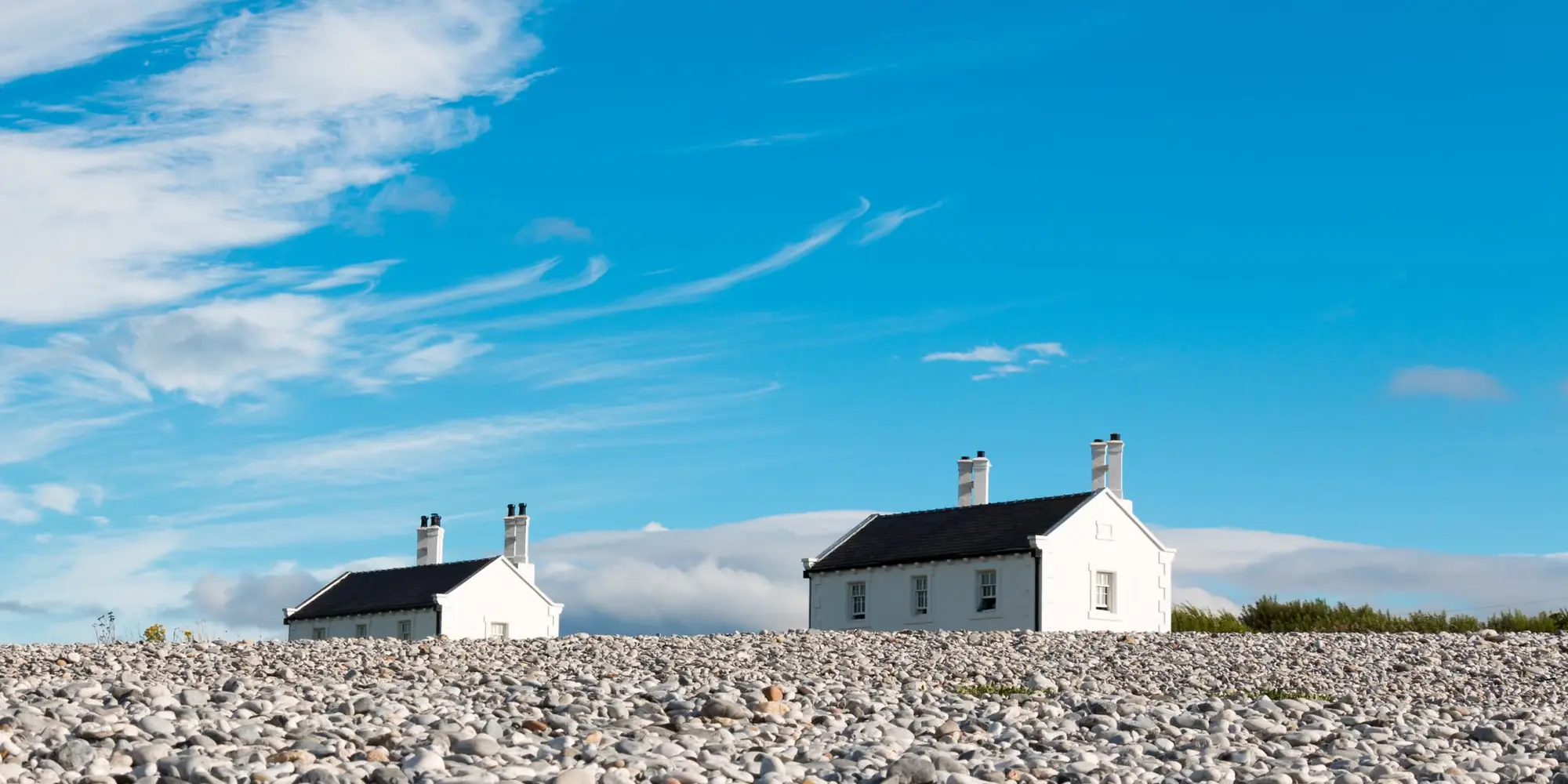 Whitewashed roughcast cottages by a shingle beach under a blue sky